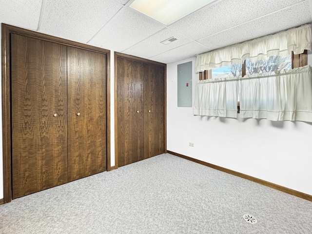 unfurnished bedroom featuring a drop ceiling, two closets, carpet floors, and electric panel