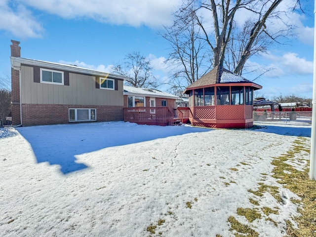 snow covered house with a wooden deck and a sunroom