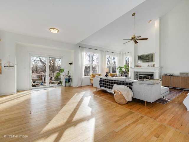 living room featuring ceiling fan, high vaulted ceiling, a tile fireplace, and light wood-type flooring