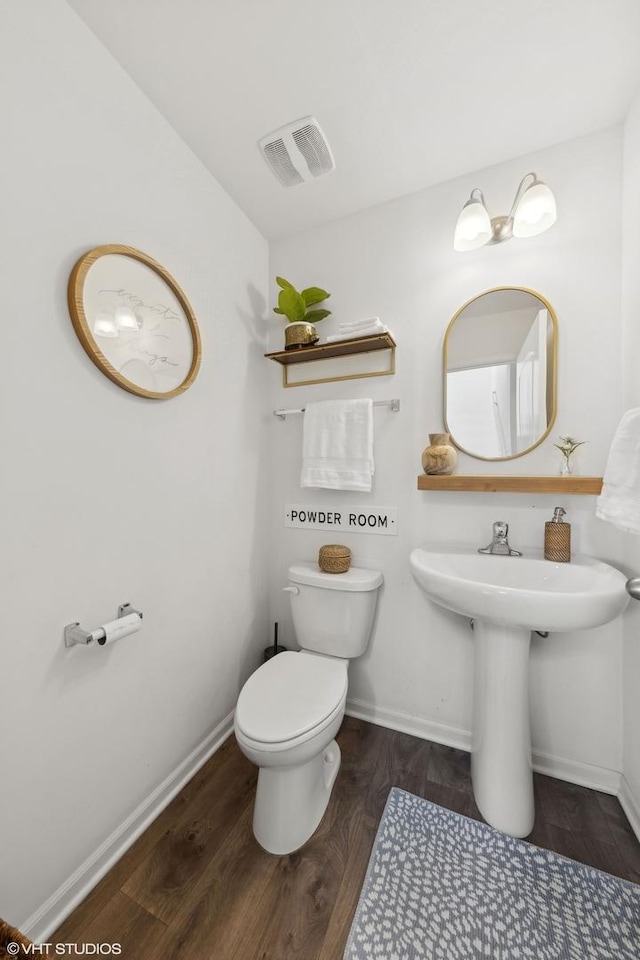 half bath with toilet, baseboards, visible vents, and wood finished floors