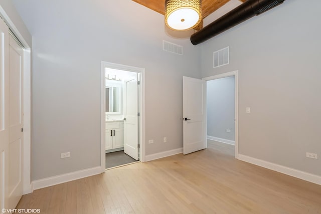 unfurnished bedroom featuring visible vents, baseboards, light wood-style floors, and a towering ceiling