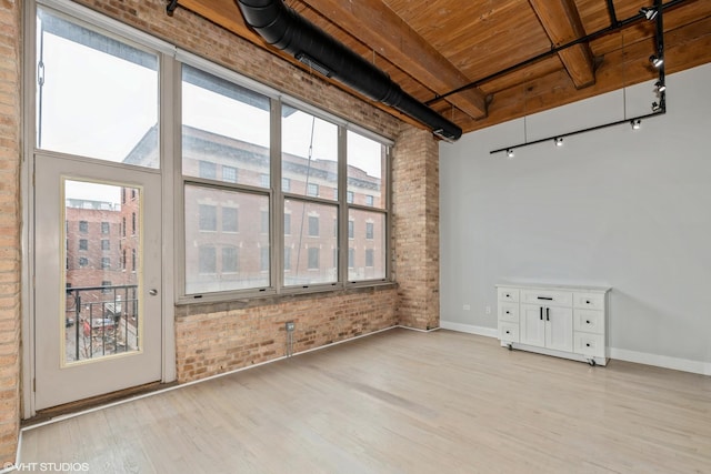 unfurnished room featuring light wood finished floors, beamed ceiling, brick wall, and baseboards