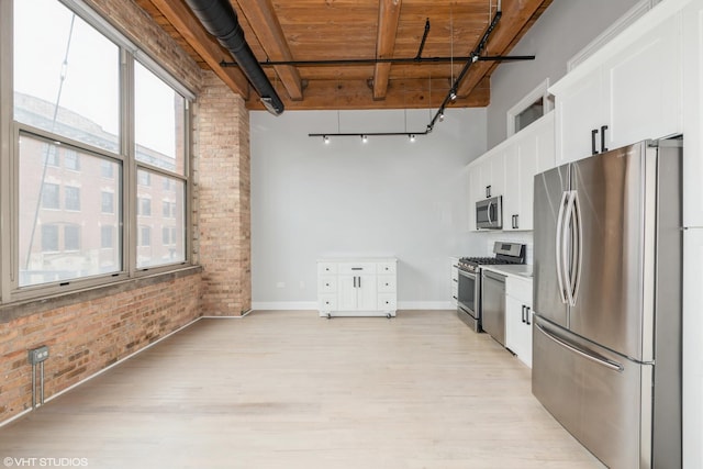 kitchen with brick wall, a high ceiling, stainless steel appliances, track lighting, and white cabinets