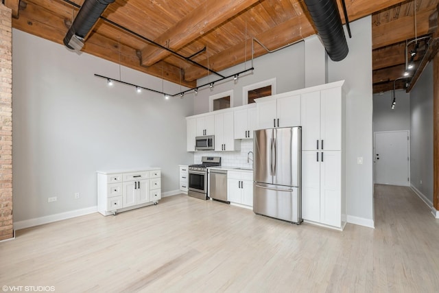 kitchen with light wood-style floors, appliances with stainless steel finishes, wooden ceiling, decorative backsplash, and a towering ceiling