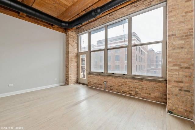 spare room featuring beam ceiling, wood finished floors, brick wall, wooden ceiling, and baseboards