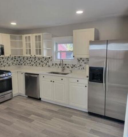 kitchen with sink, appliances with stainless steel finishes, light hardwood / wood-style floors, decorative backsplash, and white cabinets