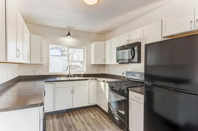 kitchen featuring dark countertops, wood finished floors, black appliances, white cabinetry, and a sink