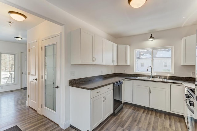 kitchen with dark wood-style floors, dark countertops, white cabinetry, a sink, and dishwashing machine