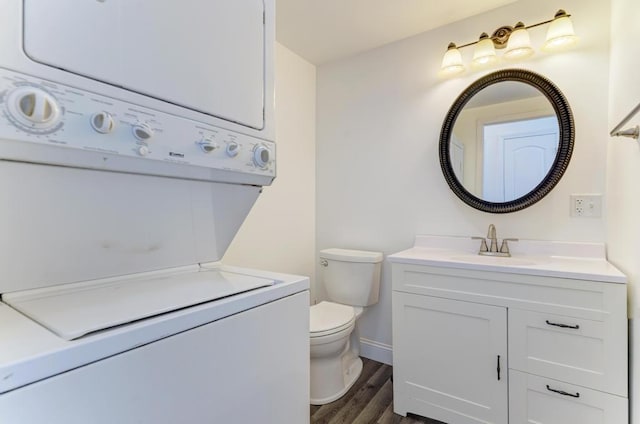 bathroom featuring toilet, stacked washing maching and dryer, wood finished floors, and vanity