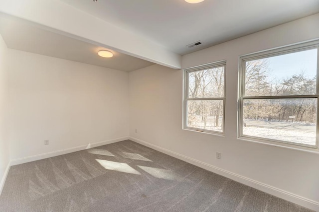 empty room featuring beamed ceiling, carpet, visible vents, and baseboards