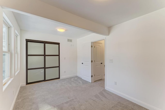 empty room featuring light colored carpet, visible vents, and baseboards