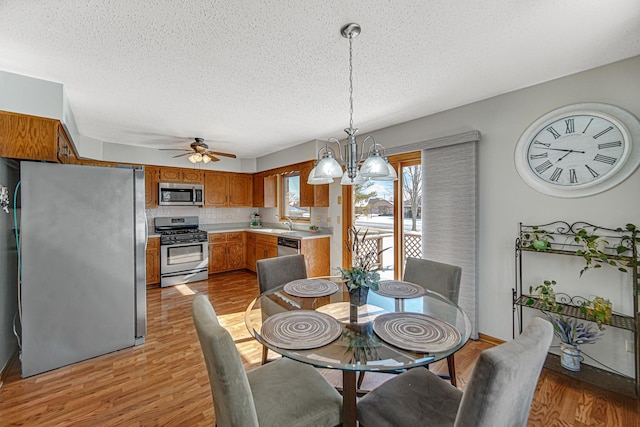 dining space featuring a textured ceiling, ceiling fan with notable chandelier, sink, and light hardwood / wood-style flooring