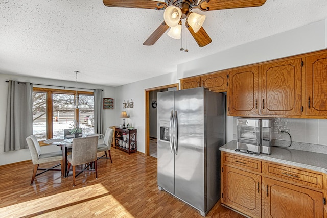 kitchen with light hardwood / wood-style flooring, a textured ceiling, stainless steel refrigerator with ice dispenser, decorative backsplash, and pendant lighting