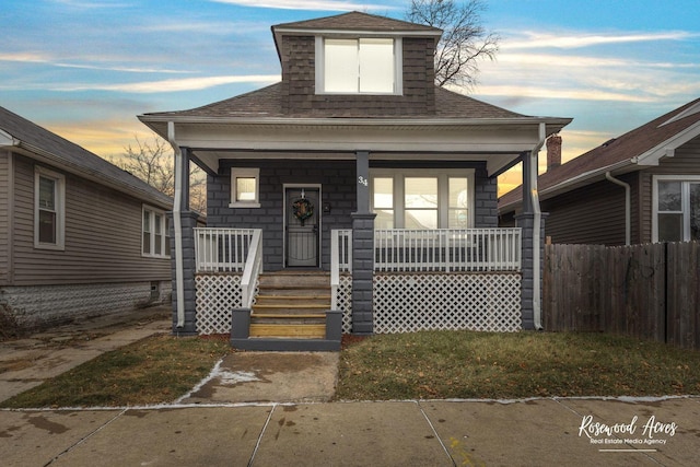 view of front of house with covered porch, a shingled roof, and fence