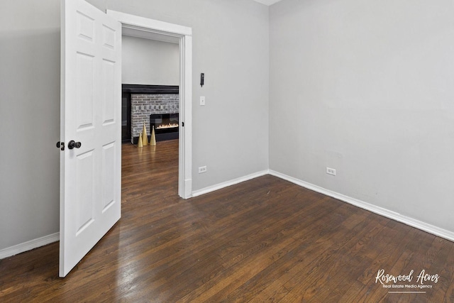 unfurnished room with dark wood-type flooring and a brick fireplace