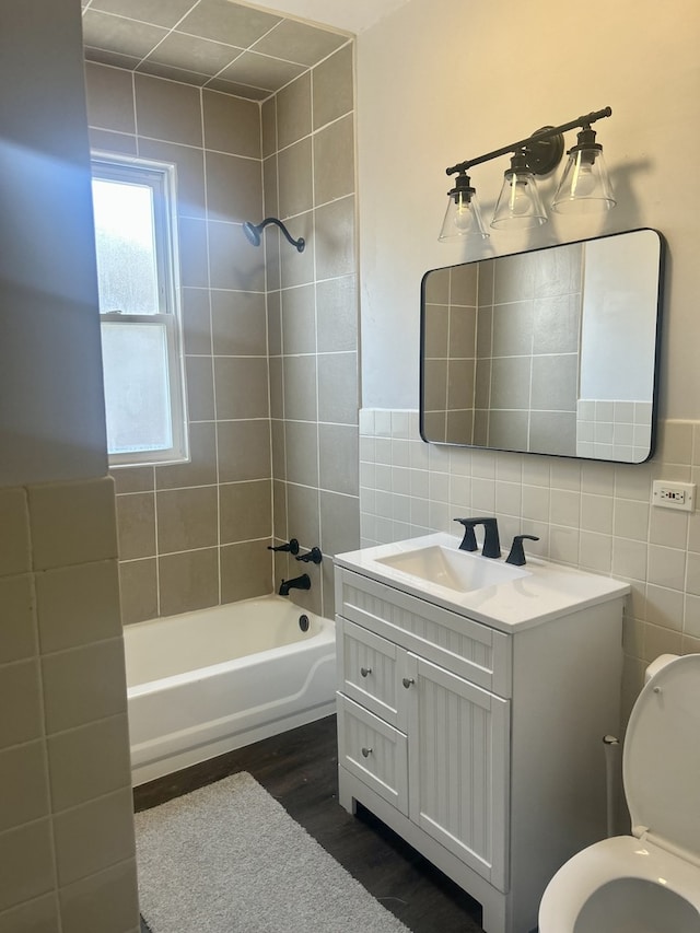 bathroom with tile walls, toilet, tub / shower combination, vanity, and wood finished floors