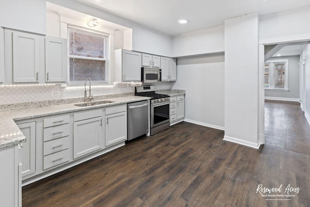 kitchen featuring appliances with stainless steel finishes, sink, backsplash, dark hardwood / wood-style flooring, and light stone counters