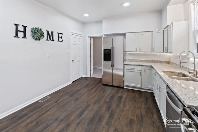 kitchen featuring appliances with stainless steel finishes, sink, dark hardwood / wood-style flooring, decorative backsplash, and light stone countertops