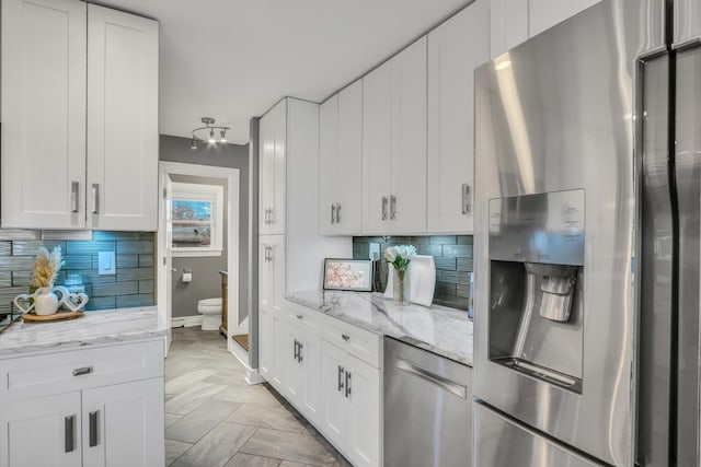 kitchen featuring stainless steel appliances, light stone countertops, white cabinets, and decorative backsplash