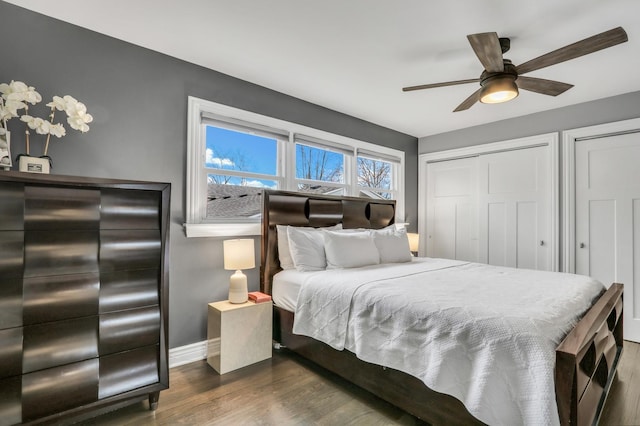 bedroom featuring ceiling fan, dark hardwood / wood-style flooring, and two closets