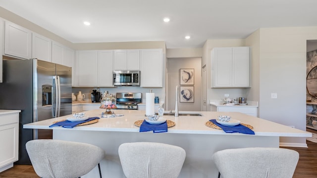 kitchen featuring stainless steel appliances, an island with sink, dark hardwood / wood-style flooring, and white cabinetry