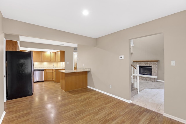 kitchen with a fireplace, light hardwood / wood-style floors, kitchen peninsula, and appliances with stainless steel finishes