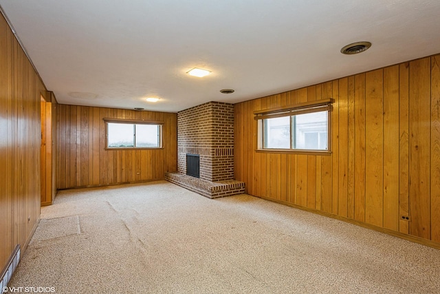 unfurnished living room with light carpet, a brick fireplace, plenty of natural light, and wood walls