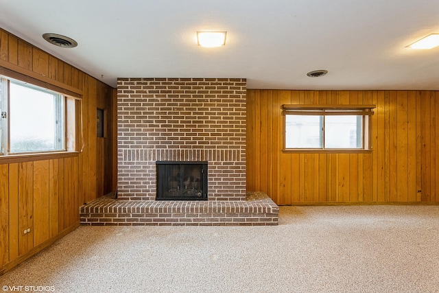 unfurnished living room with wooden walls, a healthy amount of sunlight, light colored carpet, and a fireplace