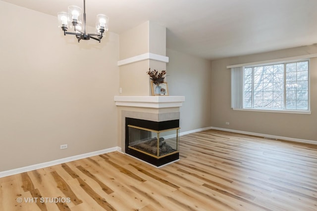 unfurnished living room with an inviting chandelier, a fireplace, and light hardwood / wood-style floors