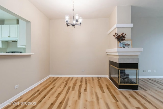 unfurnished dining area with a notable chandelier, light wood-type flooring, and a multi sided fireplace