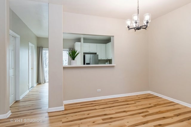 unfurnished dining area with an inviting chandelier and light wood-type flooring