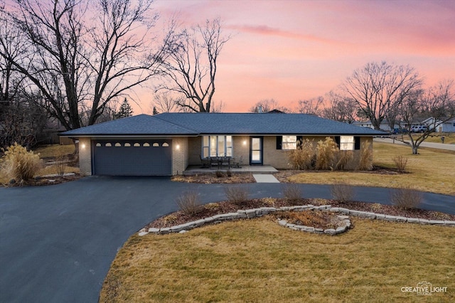 view of front of property with aphalt driveway, brick siding, a lawn, and an attached garage