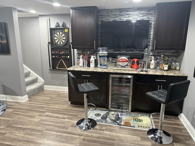 bar with backsplash, light hardwood / wood-style flooring, light stone countertops, and beverage cooler