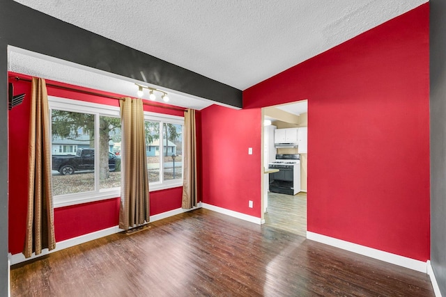 empty room with lofted ceiling, dark hardwood / wood-style floors, and a textured ceiling