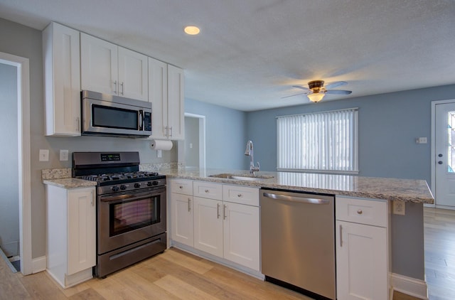 kitchen with white cabinetry, sink, kitchen peninsula, stainless steel appliances, and light wood-type flooring