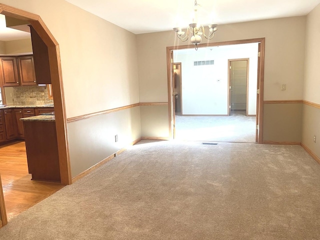 unfurnished dining area featuring light colored carpet and a notable chandelier