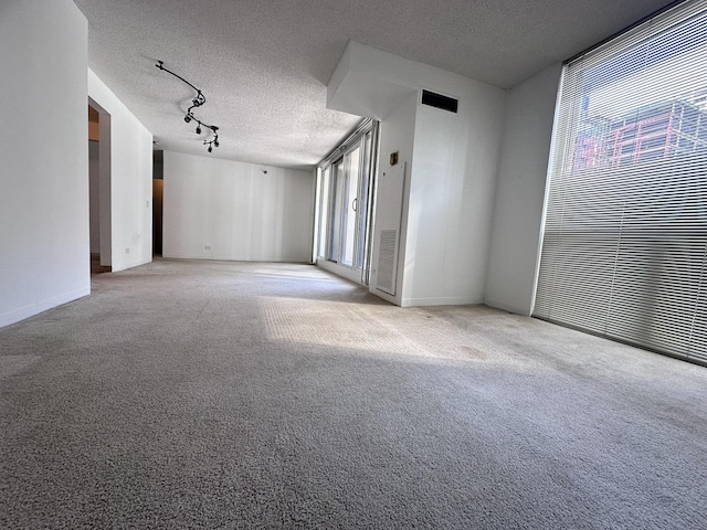 carpeted spare room featuring baseboards, visible vents, a textured ceiling, and track lighting