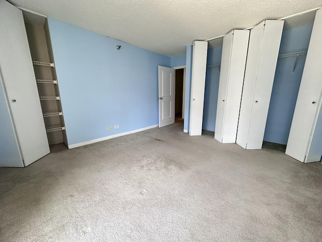 unfurnished bedroom with a textured ceiling, carpet floors, baseboards, and multiple closets