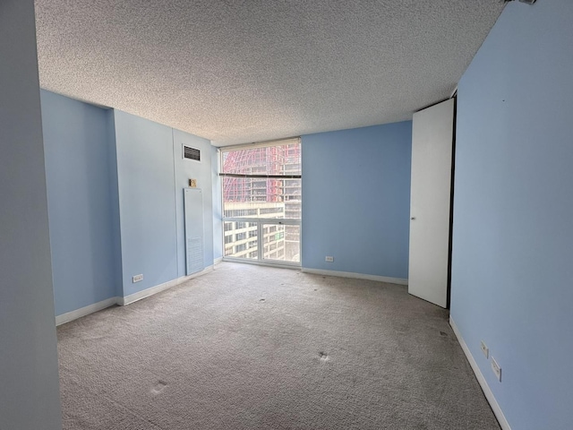 carpeted empty room with baseboards, visible vents, a wall of windows, and a textured ceiling