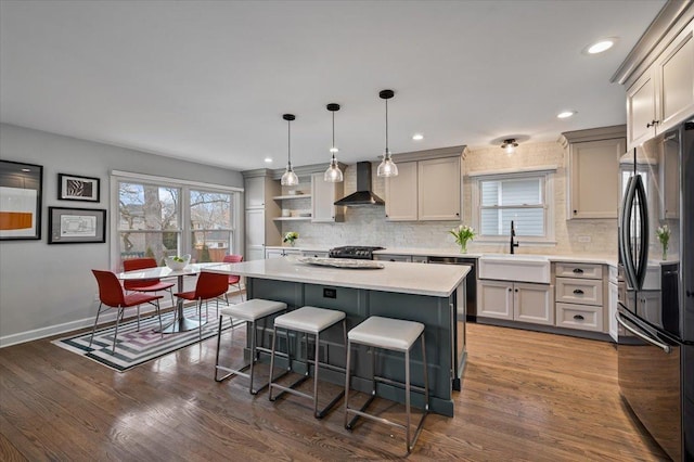 kitchen with sink, a center island, black fridge, decorative light fixtures, and wall chimney exhaust hood