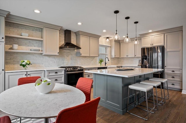 kitchen with wall chimney range hood, gray cabinets, appliances with stainless steel finishes, a kitchen island, and decorative light fixtures