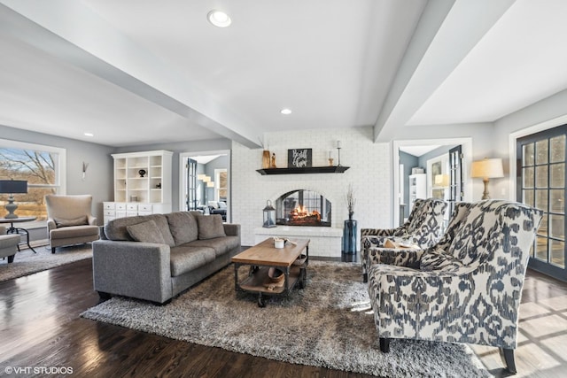 living room with hardwood / wood-style floors, beam ceiling, plenty of natural light, and a brick fireplace