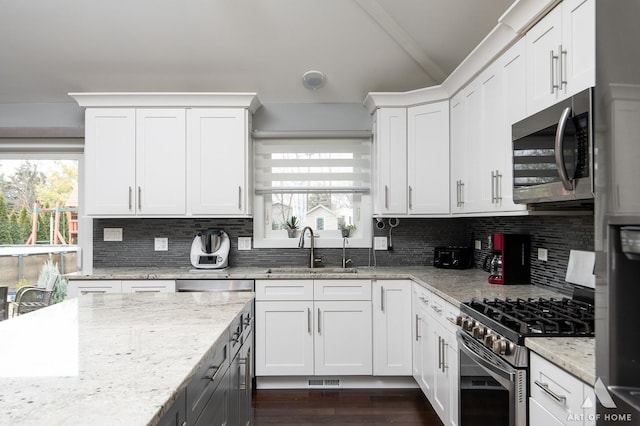 kitchen with appliances with stainless steel finishes, tasteful backsplash, white cabinetry, sink, and light stone countertops