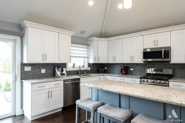 kitchen with white cabinetry, stainless steel appliances, a kitchen breakfast bar, and light stone countertops