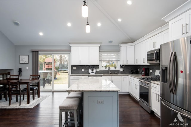 kitchen featuring white cabinetry, decorative light fixtures, a center island, vaulted ceiling, and stainless steel appliances