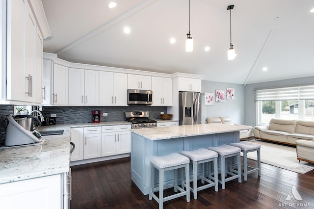 kitchen featuring a kitchen island, pendant lighting, stainless steel appliances, light stone countertops, and white cabinets