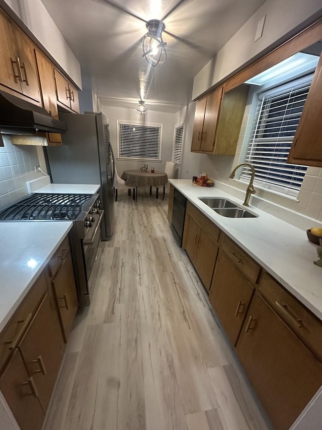 kitchen with tasteful backsplash, dishwasher, sink, stainless steel gas range, and light wood-type flooring