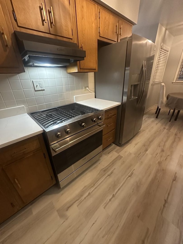 kitchen with appliances with stainless steel finishes, backsplash, and light hardwood / wood-style flooring