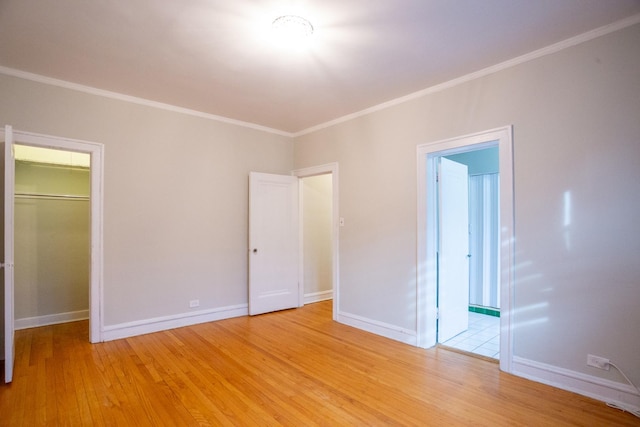 unfurnished bedroom featuring crown molding, a walk in closet, ensuite bathroom, and light wood-type flooring