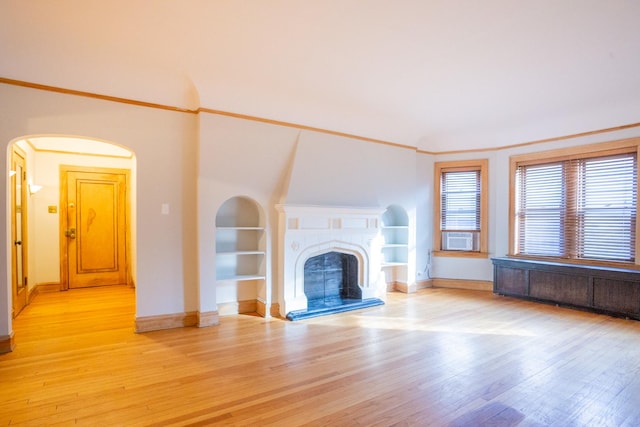 unfurnished living room featuring crown molding, built in shelves, radiator heating unit, and light wood-type flooring